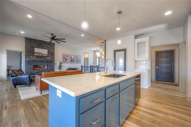 kitchen featuring light wood-style flooring, a fireplace, white cabinetry, a ceiling fan, and a sink