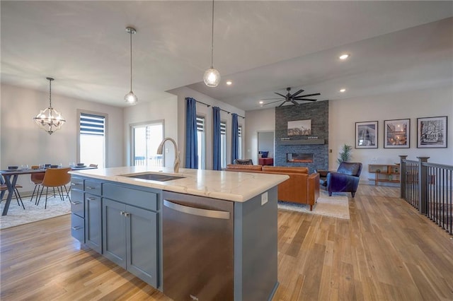 kitchen featuring a ceiling fan, a sink, a stone fireplace, light wood-style floors, and dishwasher