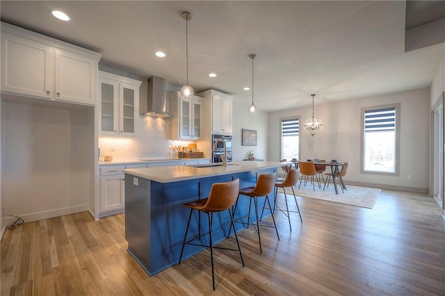 kitchen featuring a center island with sink, wall chimney exhaust hood, and white cabinetry