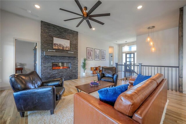 living area with recessed lighting, light wood-type flooring, a stone fireplace, and a ceiling fan