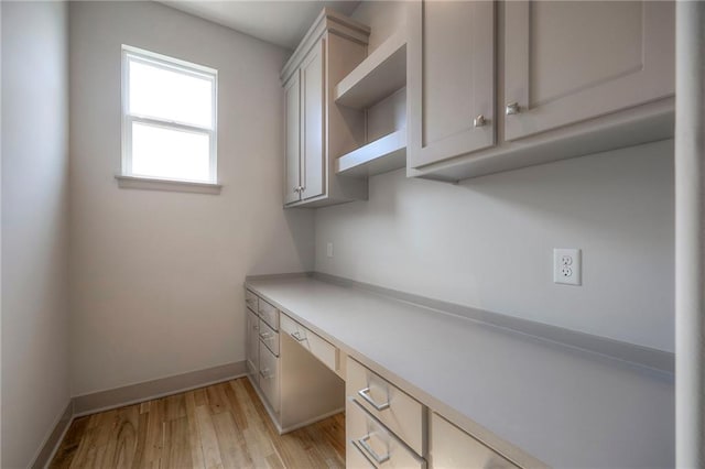 unfurnished office with baseboards, built in desk, and light wood-type flooring