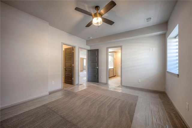 unfurnished bedroom with visible vents, baseboards, light carpet, ensuite bathroom, and a ceiling fan