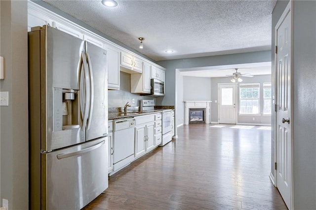 kitchen featuring dark wood finished floors, a glass covered fireplace, white cabinets, stainless steel appliances, and a ceiling fan