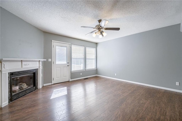 unfurnished living room featuring a ceiling fan, a textured ceiling, a glass covered fireplace, baseboards, and dark wood-style flooring