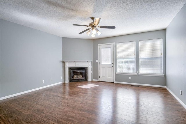 unfurnished living room featuring a glass covered fireplace, dark wood-type flooring, and ceiling fan