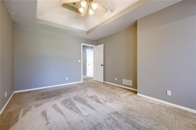 carpeted spare room with a raised ceiling, baseboards, visible vents, and ceiling fan