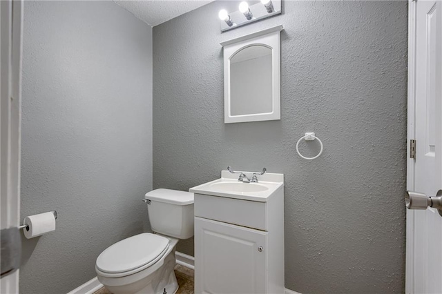 half bathroom with toilet, vanity, baseboards, and a textured wall