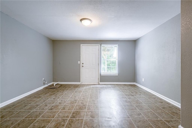 tiled empty room with baseboards and a textured ceiling