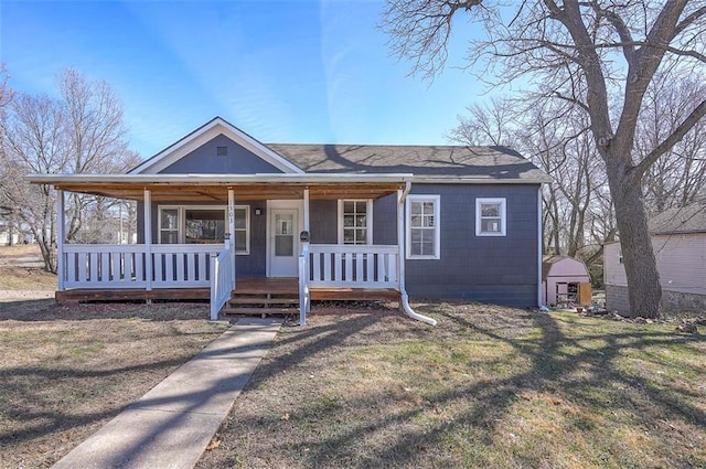 view of front of property featuring a storage unit, an outbuilding, a porch, a front yard, and a shingled roof