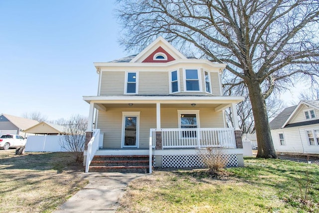 american foursquare style home featuring covered porch, a front lawn, and fence