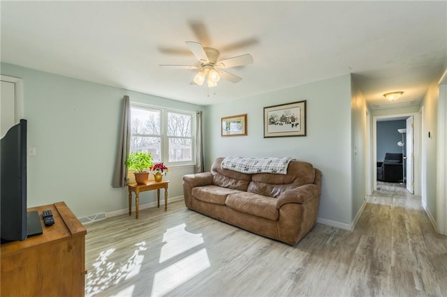 living room featuring visible vents, baseboards, a ceiling fan, and light wood finished floors