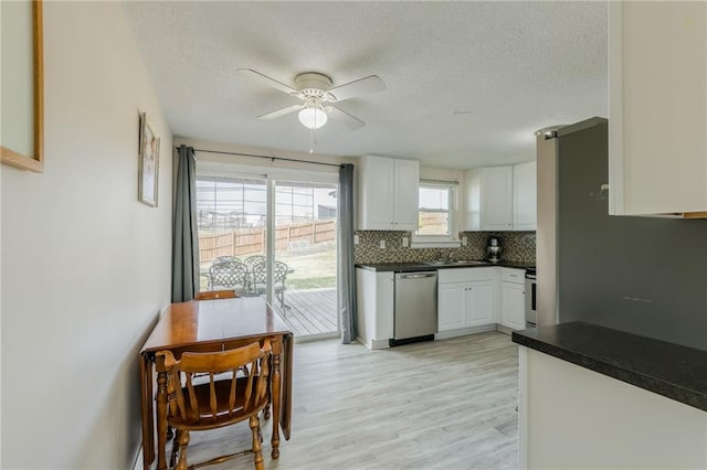 kitchen featuring a ceiling fan, backsplash, stainless steel dishwasher, dark countertops, and white cabinetry