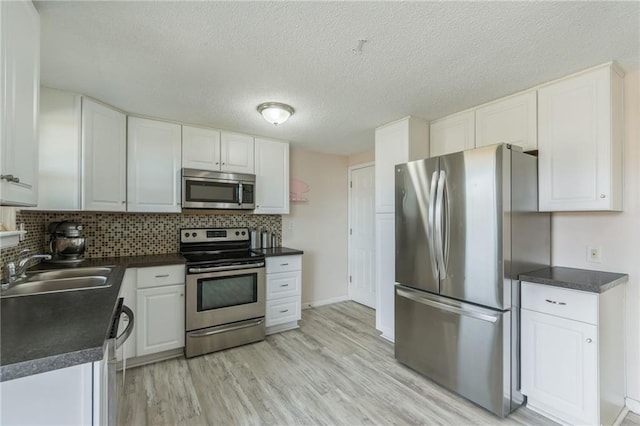 kitchen with a sink, stainless steel appliances, light wood-style floors, white cabinetry, and dark countertops