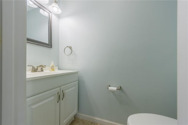 half bath featuring vanity, toilet, and baseboards