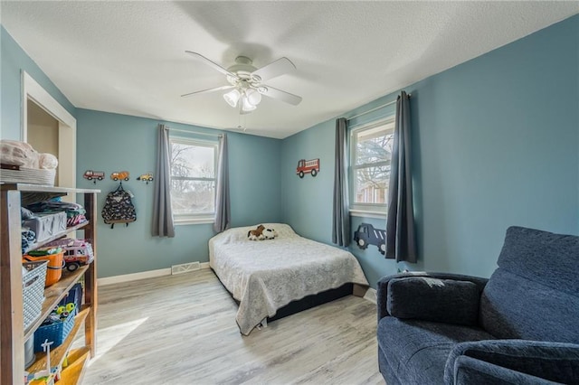 bedroom featuring light wood finished floors, visible vents, ceiling fan, baseboards, and a textured ceiling