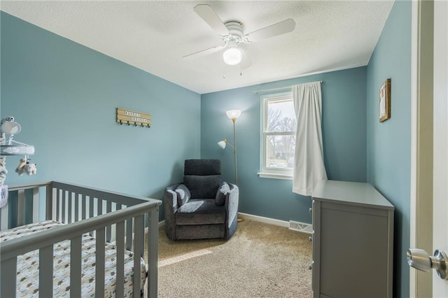 bedroom featuring visible vents, baseboards, carpet flooring, a textured ceiling, and a nursery area