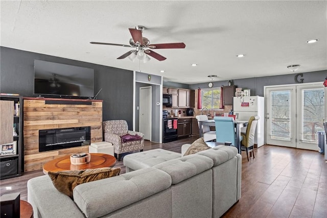 living area with ceiling fan, recessed lighting, dark wood-style floors, a glass covered fireplace, and a textured ceiling