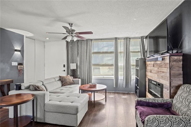 living area with a glass covered fireplace, a textured ceiling, wood-type flooring, and ceiling fan