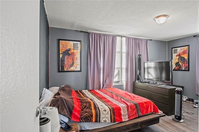 bedroom featuring a textured ceiling, a textured wall, and wood finished floors