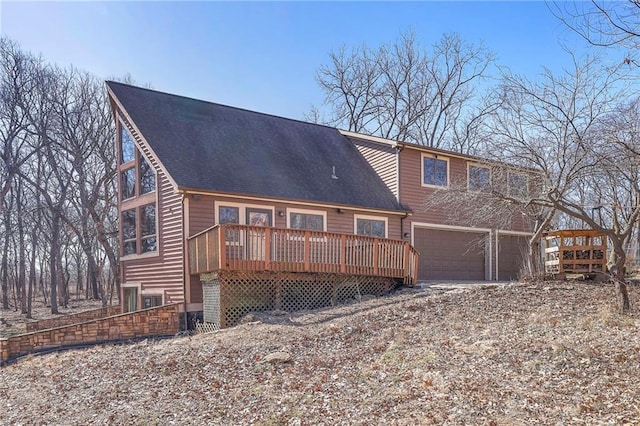 back of property featuring a deck, an attached garage, and a shingled roof