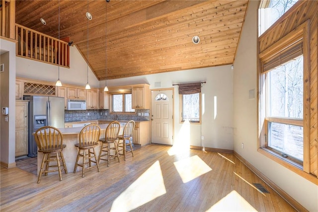 kitchen featuring white microwave, visible vents, stainless steel fridge with ice dispenser, light wood-style flooring, and high vaulted ceiling