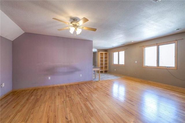 unfurnished living room with baseboards, light wood finished floors, and a textured ceiling