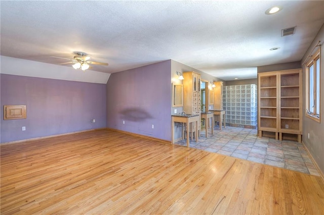 spare room featuring a ceiling fan, wood finished floors, visible vents, lofted ceiling, and a textured ceiling