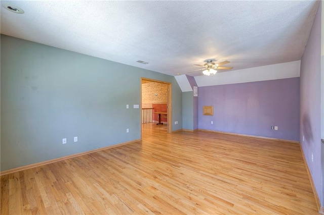 unfurnished room with visible vents, vaulted ceiling, light wood-style floors, a textured ceiling, and a ceiling fan