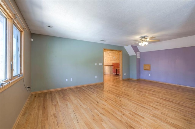 unfurnished room with baseboards, a textured ceiling, light wood-style flooring, and vaulted ceiling