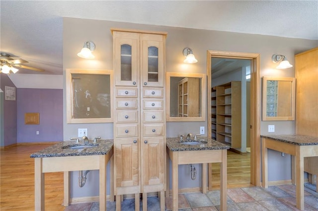 kitchen with a textured ceiling, dark stone countertops, light wood-type flooring, and a sink