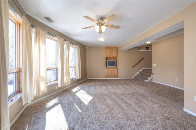 unfurnished living room featuring a wealth of natural light, visible vents, carpet flooring, and stairs