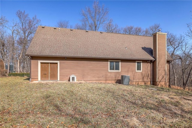 rear view of house with cooling unit, a yard, roof with shingles, and a chimney