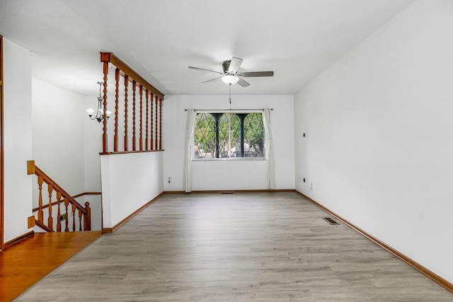 empty room with visible vents, baseboards, wood finished floors, and ceiling fan with notable chandelier