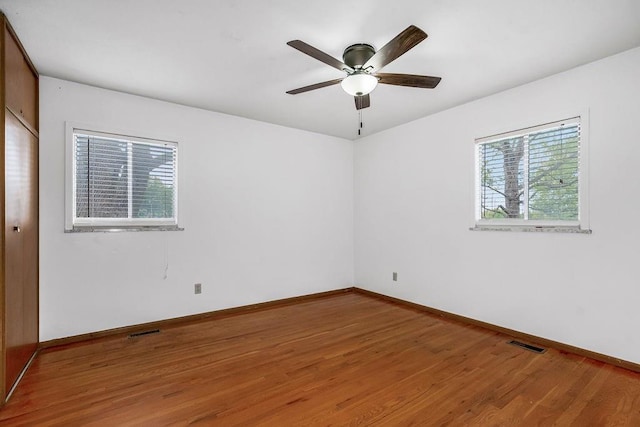 spare room with ceiling fan, wood finished floors, visible vents, and baseboards