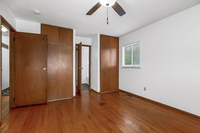 unfurnished bedroom featuring visible vents, two closets, baseboards, wood finished floors, and a ceiling fan