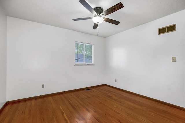 empty room featuring a ceiling fan, wood finished floors, visible vents, and baseboards