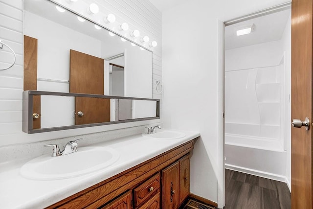 full bath featuring double vanity, wood finished floors, baseboards, and a sink