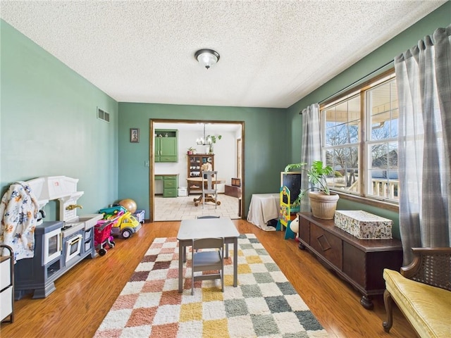 rec room with visible vents, a notable chandelier, wood finished floors, and a textured ceiling