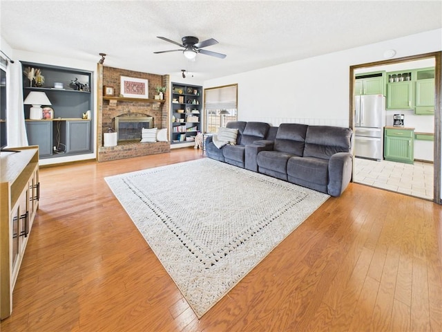 living room with built in features, light wood-type flooring, a textured ceiling, and a fireplace