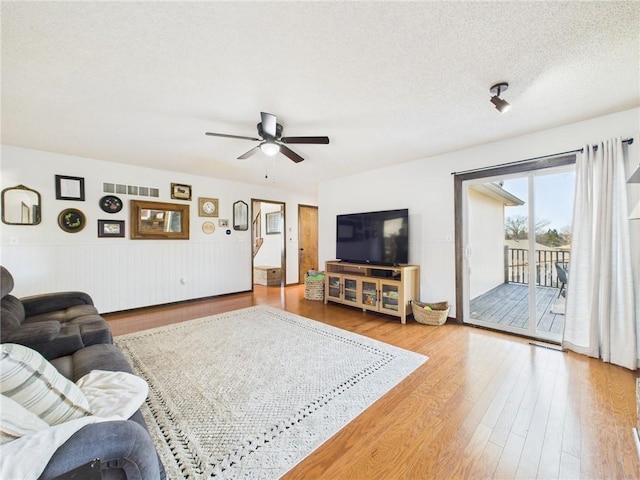 living area featuring ceiling fan, wood finished floors, wainscoting, and a textured ceiling