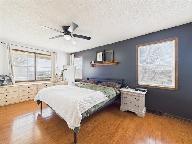 bedroom featuring a ceiling fan, baseboards, visible vents, a textured ceiling, and light wood-type flooring