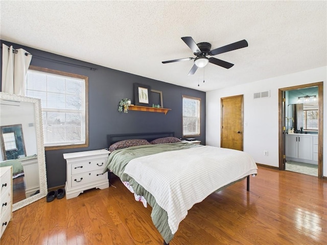 bedroom with baseboards, visible vents, hardwood / wood-style flooring, a textured ceiling, and connected bathroom