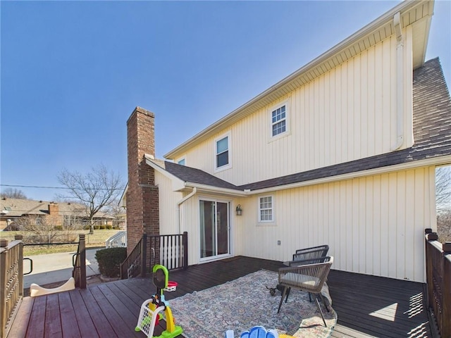 back of property featuring a chimney, a deck, and a shingled roof