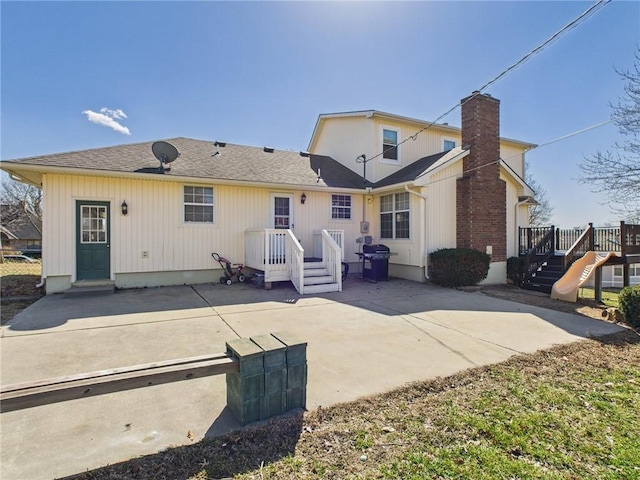 rear view of property with a wooden deck, a patio, and a shingled roof