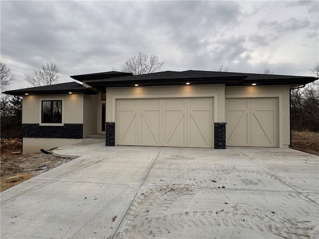 prairie-style house featuring stone siding, stucco siding, driveway, and an attached garage