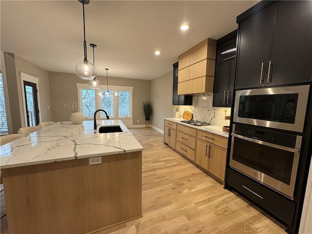 kitchen featuring tasteful backsplash, oven, built in microwave, an island with sink, and a sink