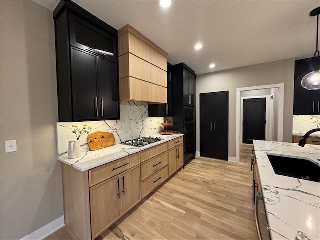 kitchen featuring gas stovetop, dark cabinets, backsplash, and a sink