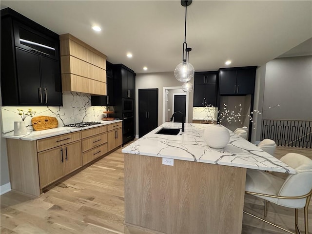 kitchen with a sink, light stone countertops, light wood-style floors, and dark cabinets