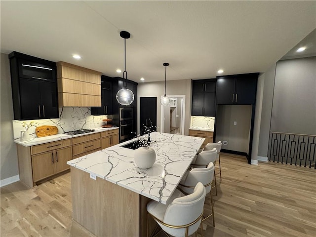 kitchen with backsplash, a center island with sink, light wood-style flooring, recessed lighting, and dark cabinetry