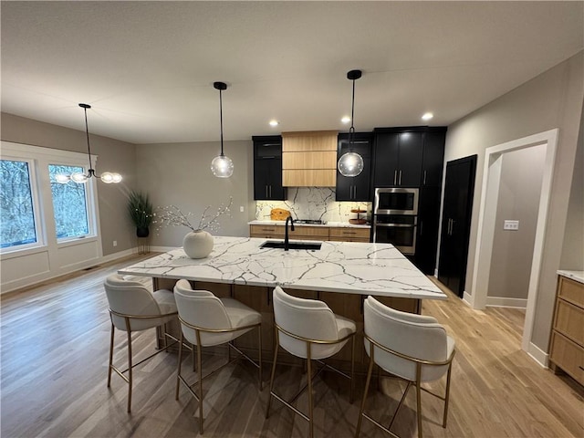 kitchen featuring dark cabinetry, a breakfast bar area, a sink, stainless steel appliances, and tasteful backsplash